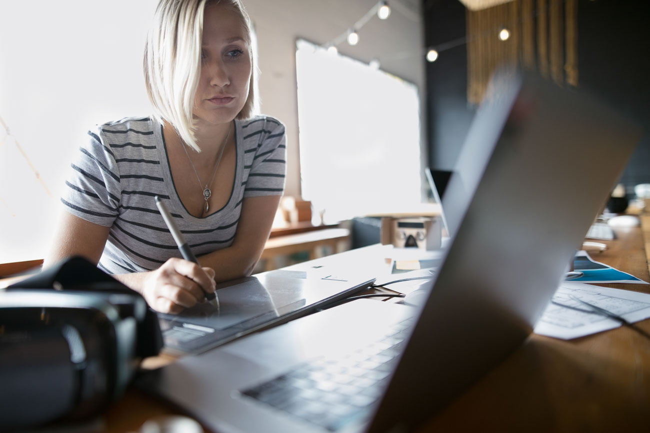focused female designer using graphics tablet at laptop in office